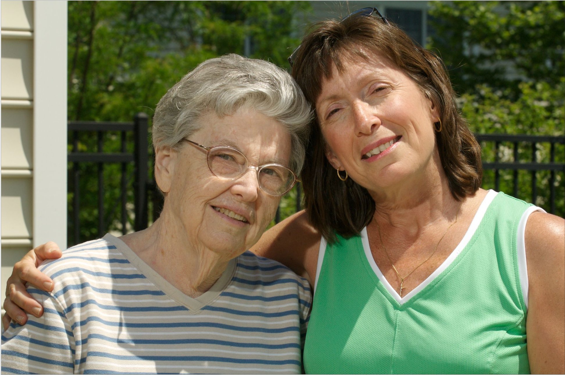 An older woman and a younger woman standing outside smiling and enjoying each other’s company.