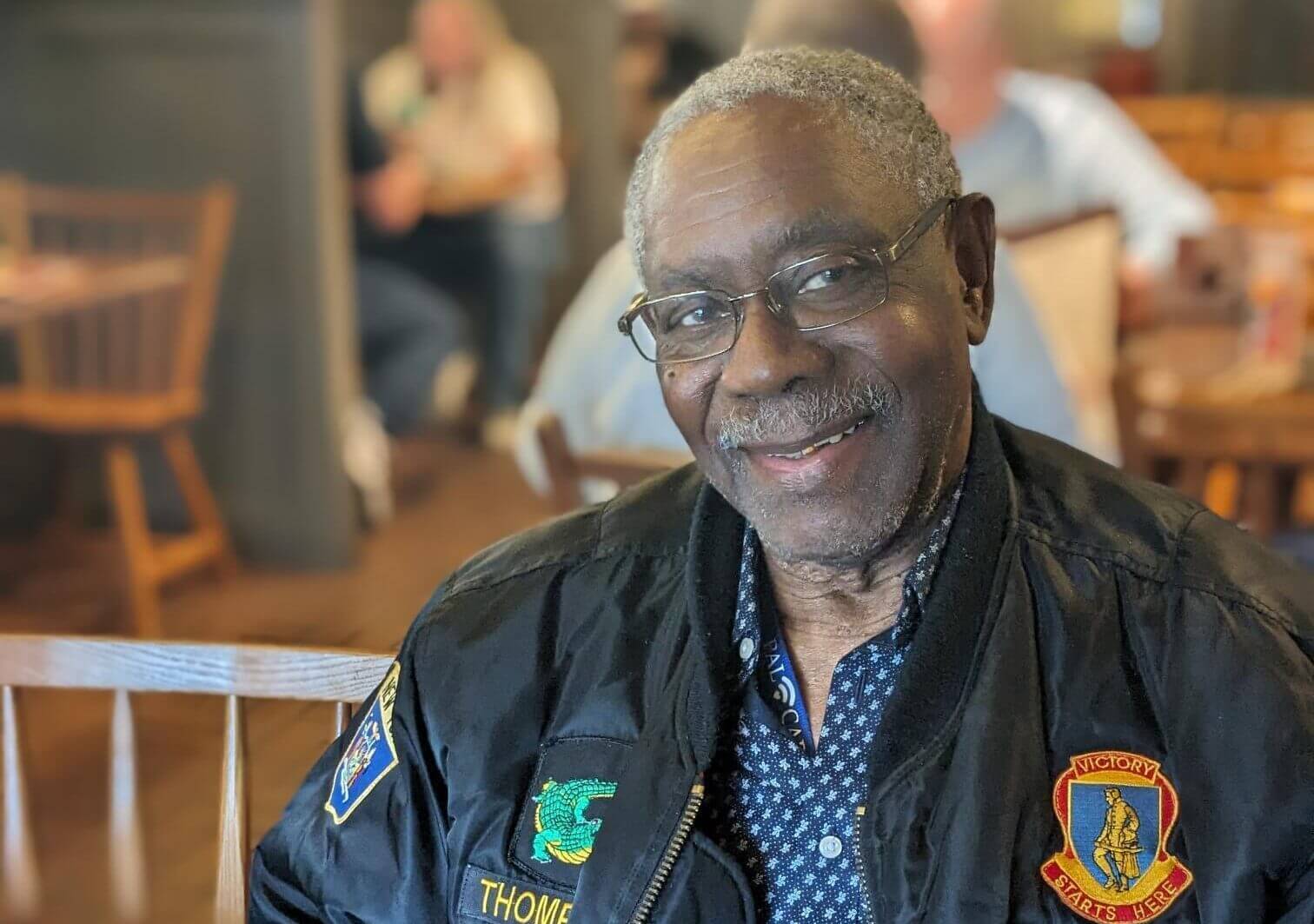Older man smiling while wearing a military jacket.